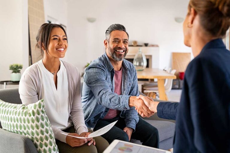 A couple and a real estate agent reviewing documents and signing papers at a table inside a home.